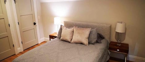 Un dormitorio con una cama, dos mesitas de noche, una lámpara y una puerta.