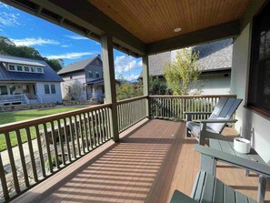Eine überdachte Veranda mit Holzterrasse, einer Bank und Blick auf benachbarte Häuser.