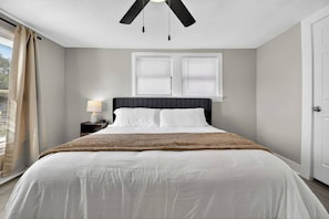 A bedroom with a bed, a nightstand, a lamp, a ceiling fan, and two windows with blinds. - Minimalist Escape | 12 mins to Downtown Houston (Houston)