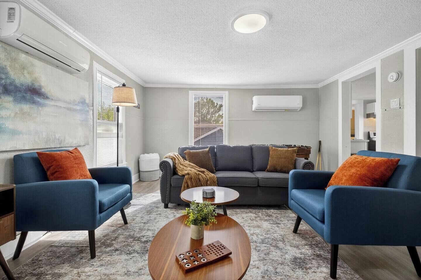 Un salon moderne avec un canapé gris, des fauteuils bleus, une table basse et un tableau accroché au mur.