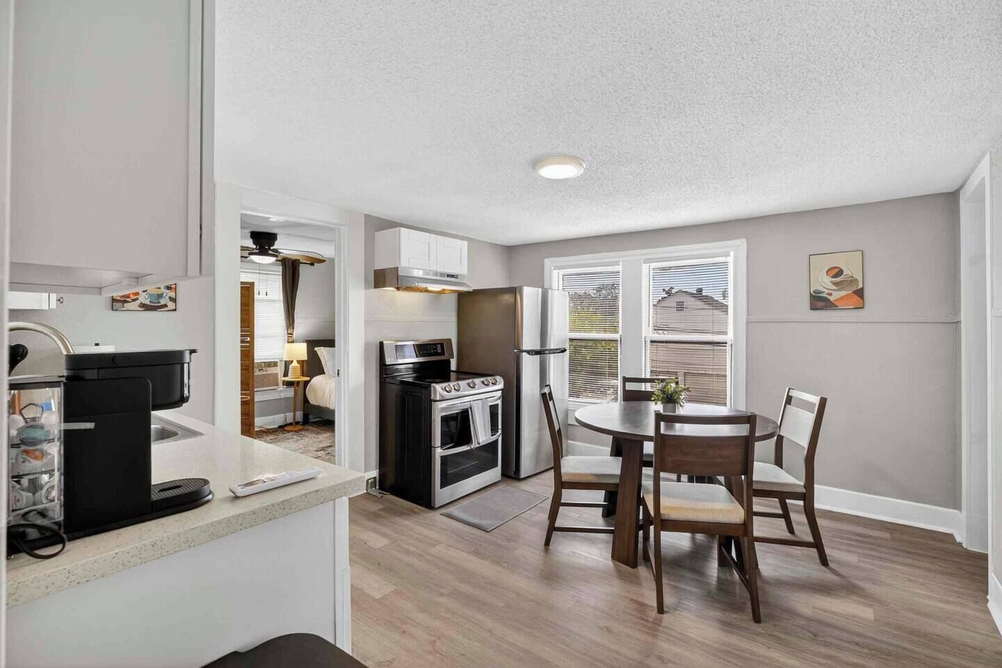 A compact kitchen with a stove, oven, and refrigerator, a dining table with chairs, and a window with blinds.