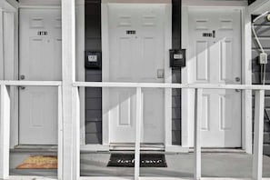 Un edificio con tres puertas blancas, cada una con un número. Hay un buzón negro sujeto a la pared entre las puertas.