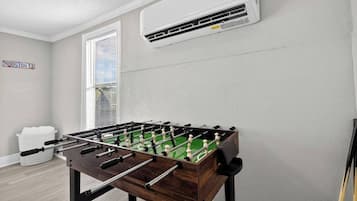 Een kamer met een tafelvoetbaltafel, een raam met zonwering, een luchtverkoeler aan de muur en een bord waarop 'HOUSTON TX' staat.