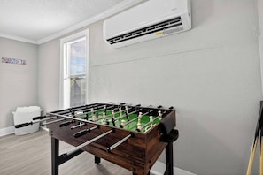 A room with a foosball table, a window with blinds, a wall-mounted air conditioner, and a sign reading 'HOUSTON TX'. - Minimalist Escape | 12 mins to Downtown Houston (Houston)