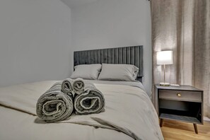 A neatly made bed with rolled towels, a bedside lamp, and a nightstand with a drawer.