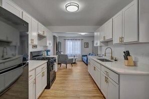 A modern kitchen with white cabinets, a stove, and a sink. There is a dining area with a table and chairs.