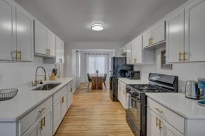 A modern kitchen with white cabinets, a wooden dining table, and a black stove. - Cozy and Full of Light: Newly Renovated 2BR Home (Detroit)