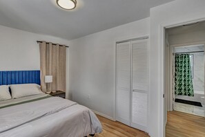 A bedroom with a bed, a nightstand, a lamp, a wardrobe, and a bathroom visible through an open door. - Cozy and Full of Light: Newly Renovated 2BR Home (Detroit)