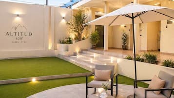 Un área de estar moderna al aire libre con una sombrilla blanca, una mesa pequeña con una taza, y un letrero que indica la altitud del hotel.