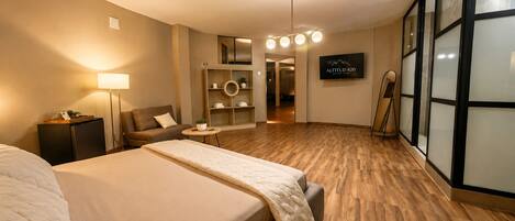 A hotel room with a bed, a sofa, a small table, a lamp, a TV, and a mirror.