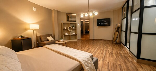 A hotel room with a bed, a sofa, a small table, a lamp, a TV, and a mirror.