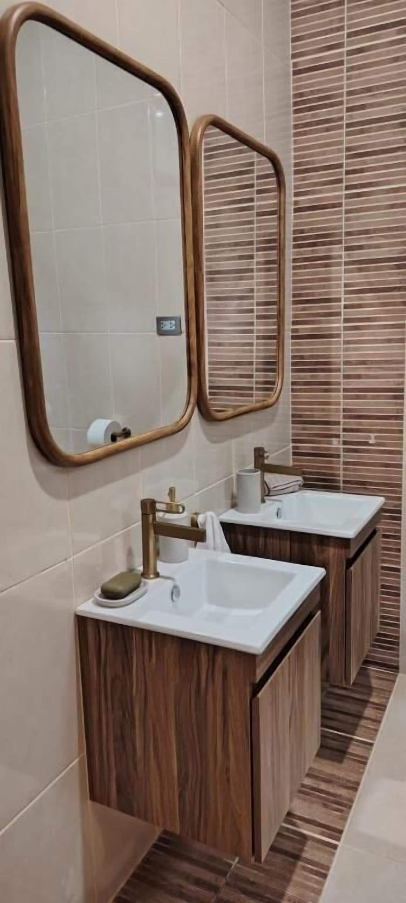Un baño con dos lavamanos, muebles de madera y dos espejos.