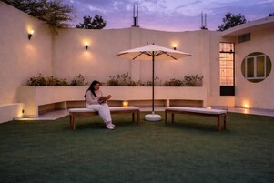 A person seated on a bench in a well-lit outdoor area with a table and an umbrella.