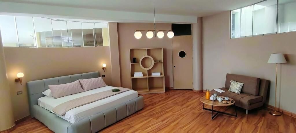 A modern bedroom with a large bed, a sofa, a small table, and a wardrobe.