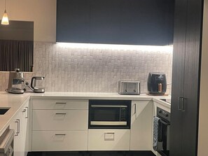 A modern kitchen with white cabinets, a microwave, a toaster, and a coffee maker. - Inviting Family Home in Queenstown. (Lake Hayes Estate)