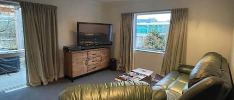 A living room with a leather sofa, a television on a wooden cabinet, and a window with curtains.