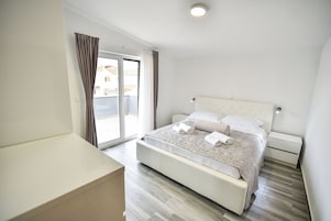 Une chambre moderne avec un grand lit, une table de chevet, une commode et une porte-fenêtre coulissante donnant sur un balcon.