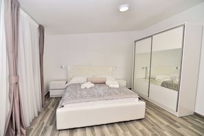 A modern bedroom with a large bed, a wardrobe, and a mirror.