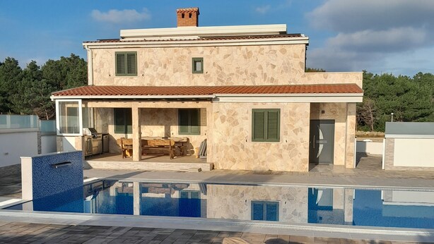 Une maison à deux étages dotée d’une piscine, de mobilier d’extérieur et d’une façade en pierre.