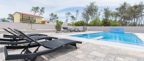 A pool area with lounge chairs and a small building in the background.