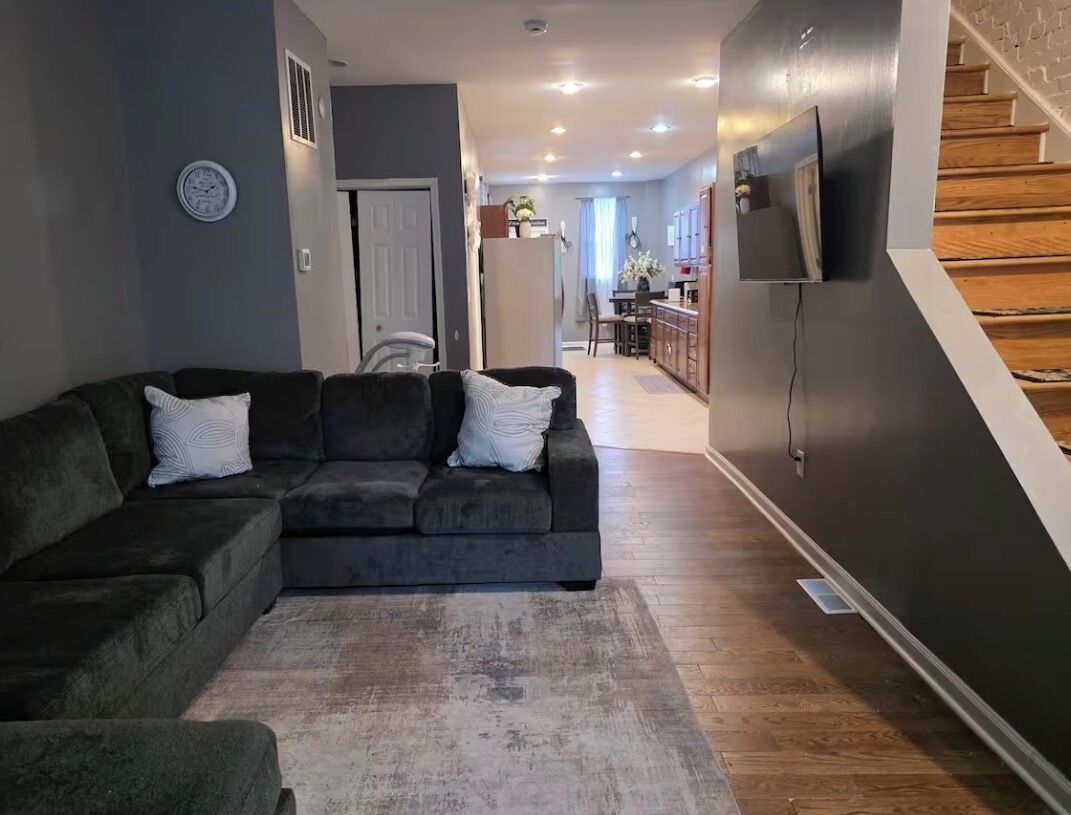A living room with a dark-colored sofa, a rug, and a television mounted on the wall.