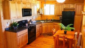 Une cuisine aménagée dans le style d’un chalet en bois, avec un poêle, un four à micro-ondes, un réfrigérateur et des placards en bois.