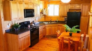 Une cuisine aménagée dans le style d’un chalet en bois, avec un poêle, un four à micro-ondes, un réfrigérateur et des placards en bois.
