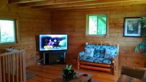 L’intérieur d’un chalet en bois, avec une télévision, un canapé, une table basse et un berceau.