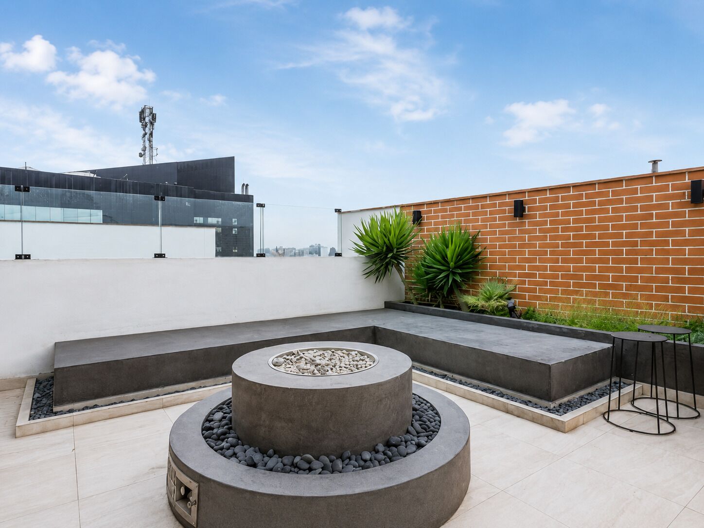 A rooftop terrace with a circular seating area, a brick wall, and a modern building in the background.