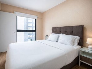 Une chambre d’hôtel avec un lit, une table de chevet, une lampe et une vue sur la ville par la fenêtre.
