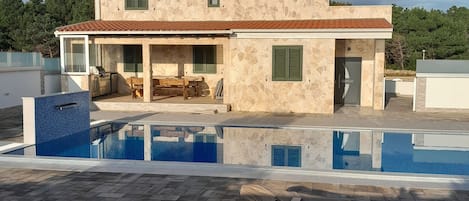 Une maison à deux étages dotée d’une piscine, de mobilier d’extérieur et d’une façade en pierre.
