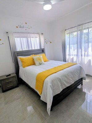 A neatly made bed with a white and yellow bedspread, a wooden headboard, and a bedside table with a drawer.