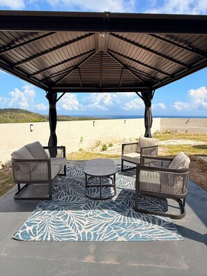 An outdoor patio with a covered seating area, a patterned rug, and a view of the landscape.