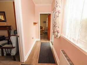 A hallway with a wooden floor, a doormat, a chair, and a door leading to another room. - GOLF CLUB VIEW, pet friendly, with open fire in Doonbeg, County Clare (County Clare)