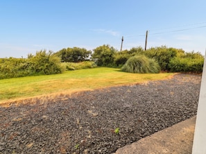 A gravel driveway leading to a grassy area with a hedge and trees in the background. - GOLF CLUB VIEW, pet friendly, with open fire in Doonbeg, County Clare (County Clare)