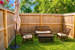 Un jardin avec une clôture en bois, une table de patio, deux chaises et un parasol.
