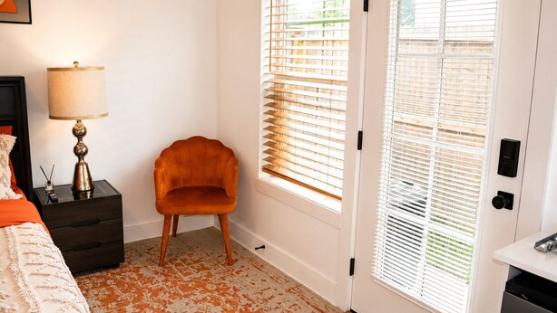 A bedroom with a bed, a nightstand with a lamp, a chair, and a door with blinds. - Luxury 1BR Private Suite • Private Entry • Houston Getaway (Houston)