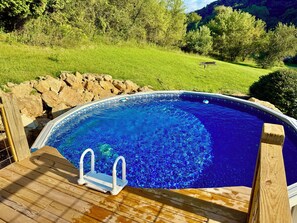 A swimming pool with a wooden deck and a view of a grassy landscape.