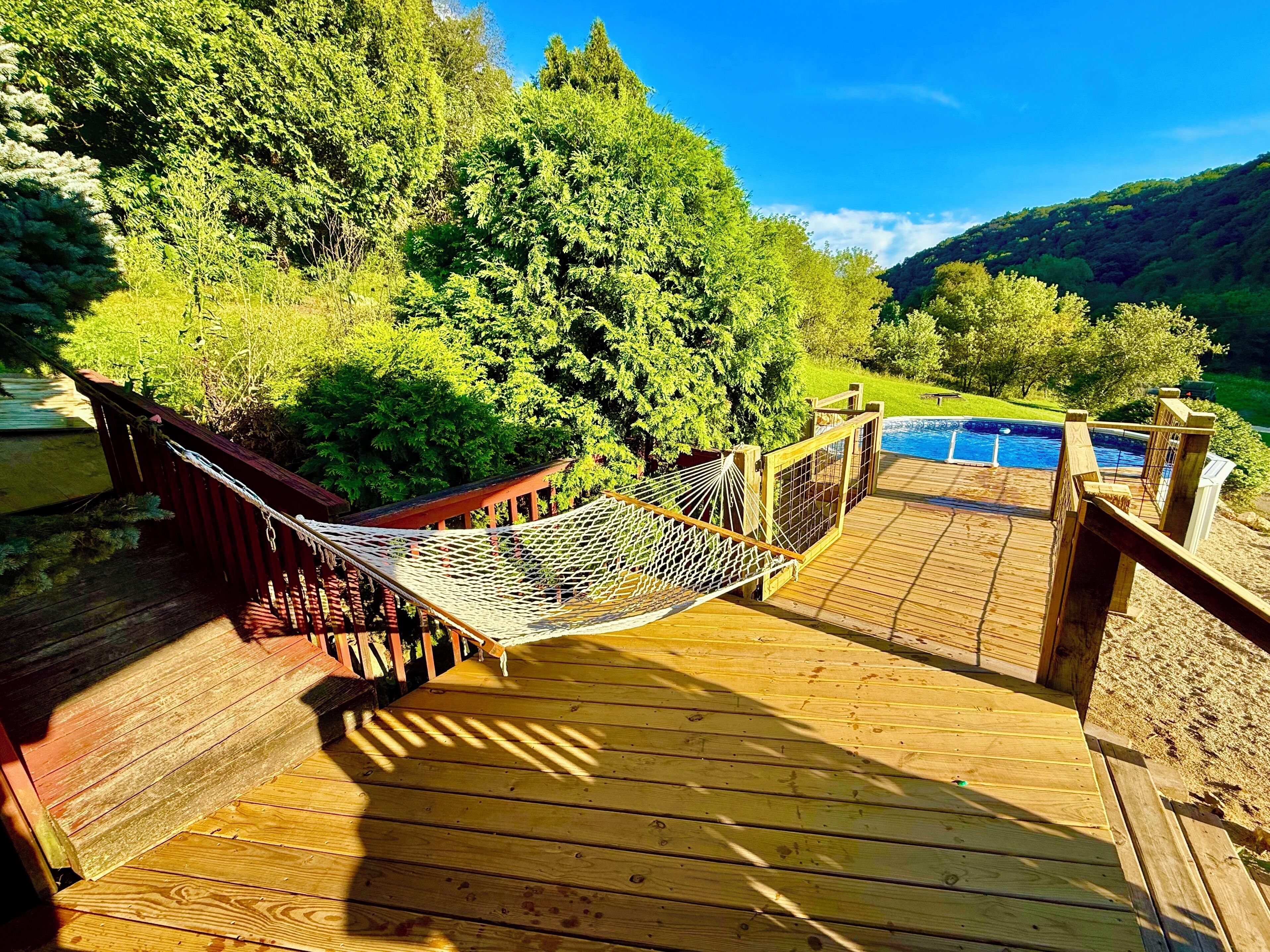 A wooden deck with a hammock, a pool, and a view of a forested hillside.