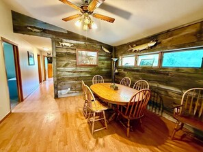 A dining area with a wooden table and chairs, a ceiling fan, and a rustic wall with mounted fish.