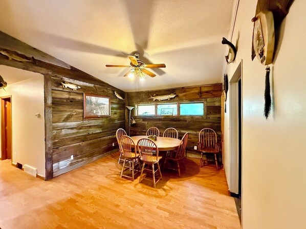 A dining area with a wooden table and chairs, a ceiling fan, and wooden walls.