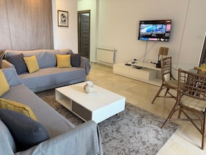 A modern living room with a grey sofa, a white coffee table, and a TV mounted on the wall. - Stylish 2BR Fully Equipped La Marsa (La Marsa)