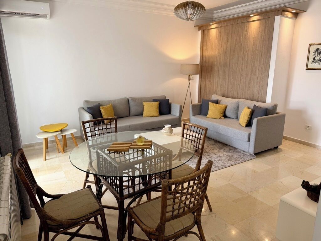 A modern living room with a glass dining table, two sofas, and a floor lamp.