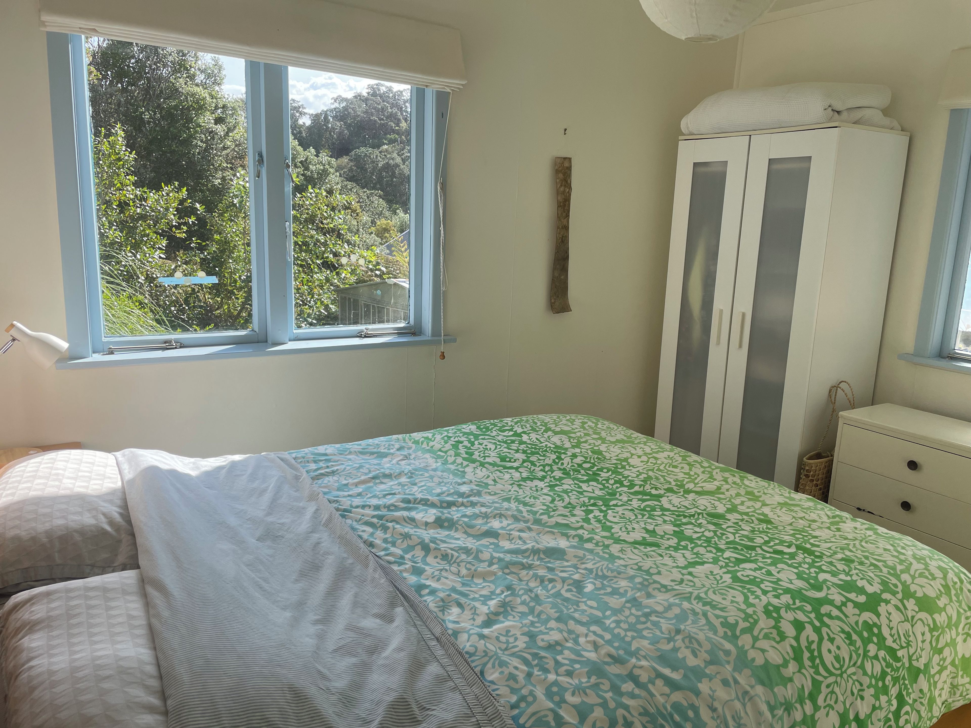 A bedroom with a bed, a wardrobe, and a window with a view of greenery.