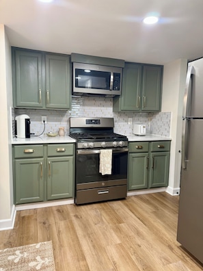 A kitchen with green cabinets, a stainless steel oven, a microwave, and a refrigerator.