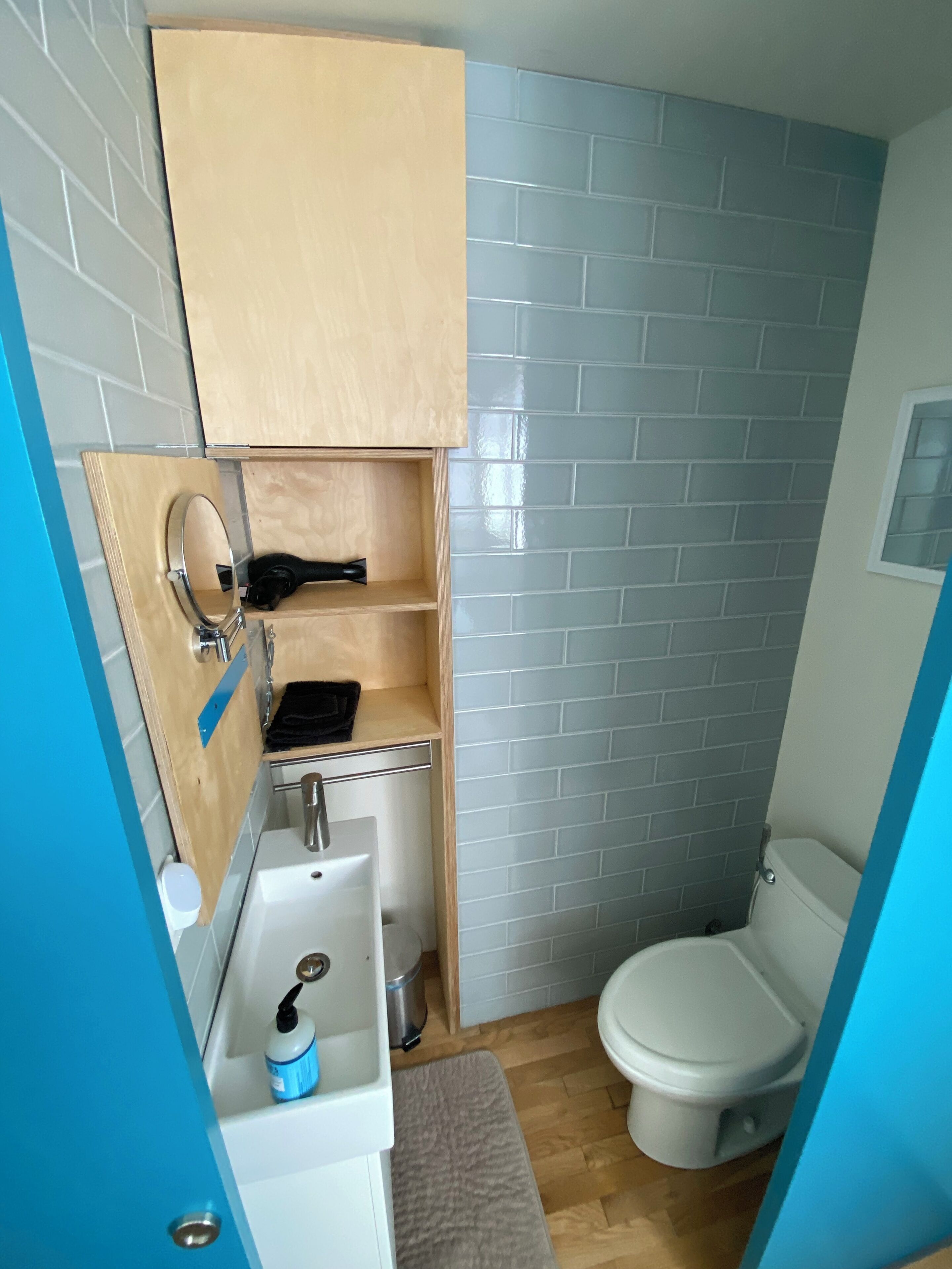 A compact bathroom with a white sink, a mirror, a toilet, and a wooden cabinet.