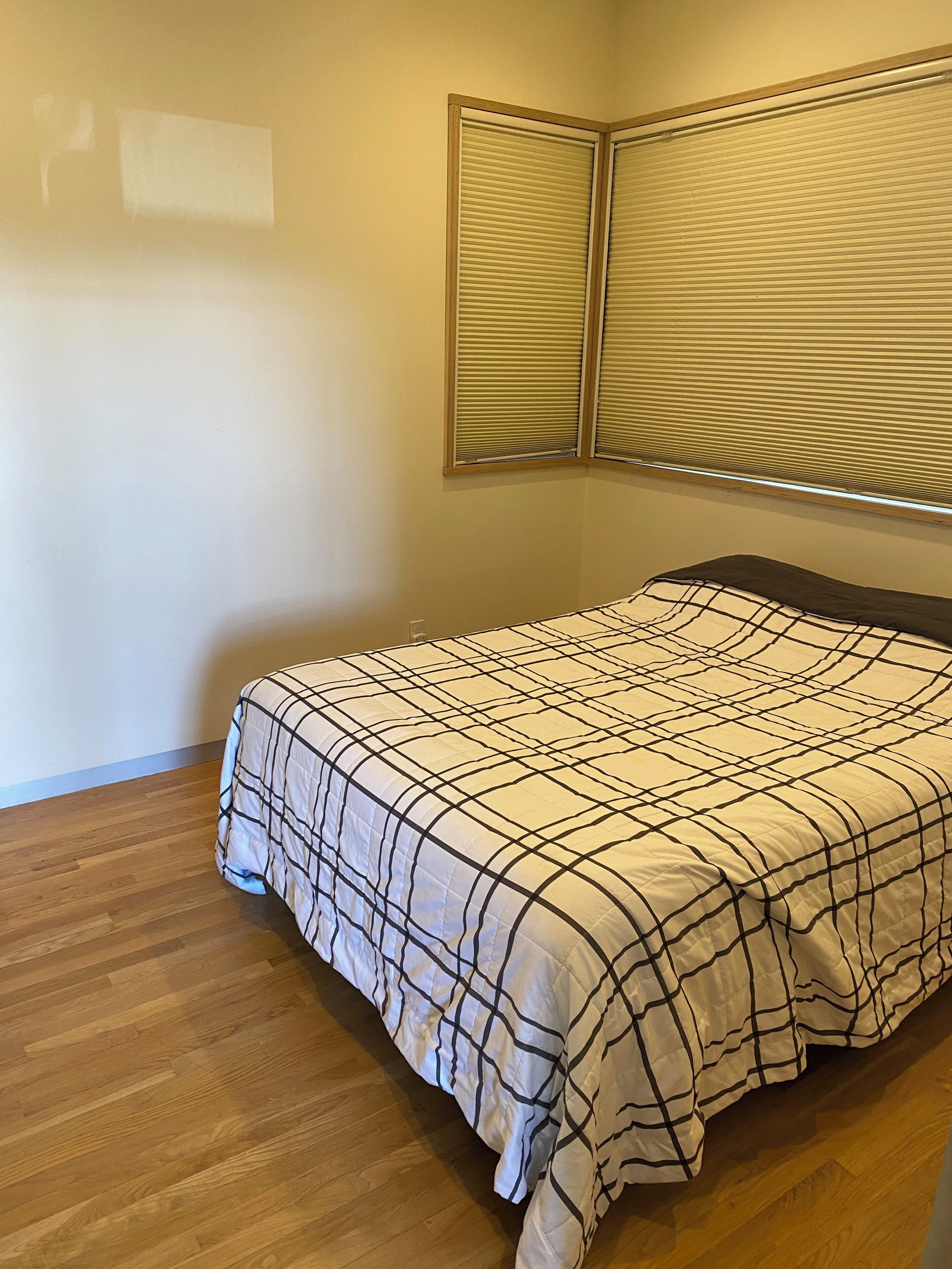 A bedroom with a bed, wooden flooring, and a window with blinds.