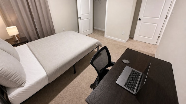 A hotel room with a single bed, a desk with a laptop, a chair, and a lamp. - Spacious 5BR Upper Home Near DC, National Harbor & Joint Base Andrews (Waldorf)