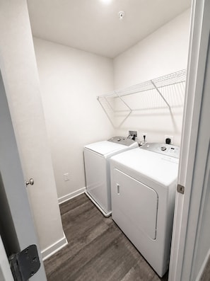 A laundry room with two white washing machines, a drying rack, and a small window.