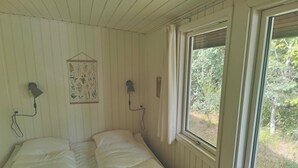 A room with a single bed, two wall-mounted lamps, a framed botanical illustration, and a window with a view of greenery. - Cozy holiday home in Hune near Blokhus (Hune)